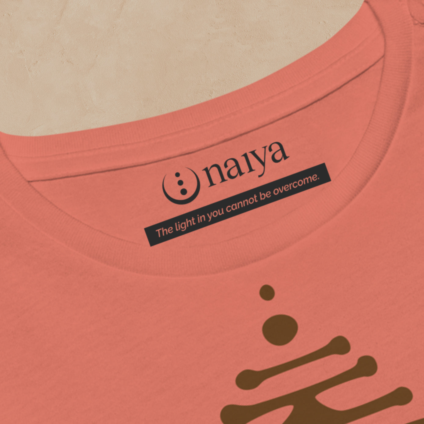 Close-up of a terracotta t-shirt with 'naiya' logo and text on a beige background